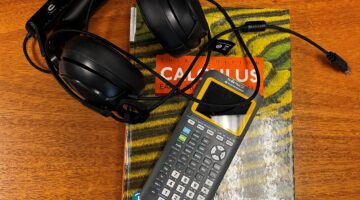 Headphones, graphing calculator, and calculus textbook on a wooden desk.