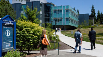 Students walking along a campus pathway near Bellevue College buildings and signage.