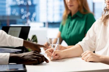 Three people sitting in a desk with faces being covered and the main focus is on their hand
