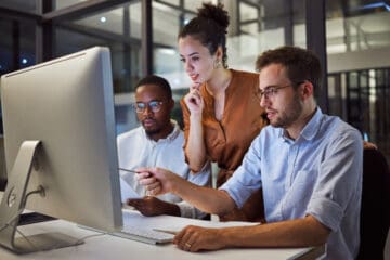 three people gathered around a computer and analyzing what they see