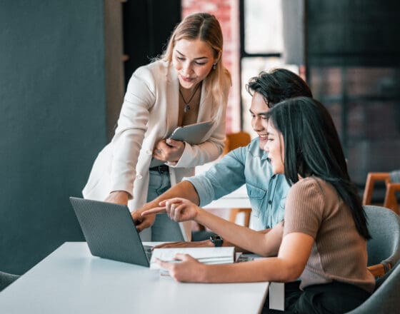 Three people dressed professionally sitting around a desk and pointing at a screen