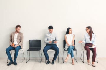 4 people sitting down with a 5th chair that is empty