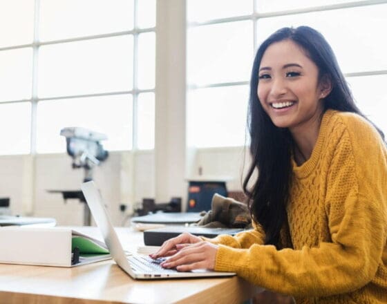 Women smiling at the camera while on her computer and sitting in desk at an office
