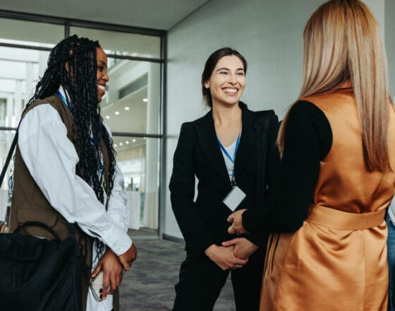three women talking to each other in a professional setting and everyone who's face is showing is smiling