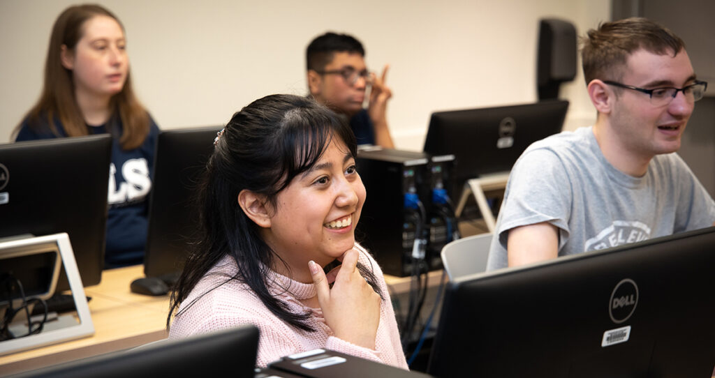 Students attend class in front of computer stations.