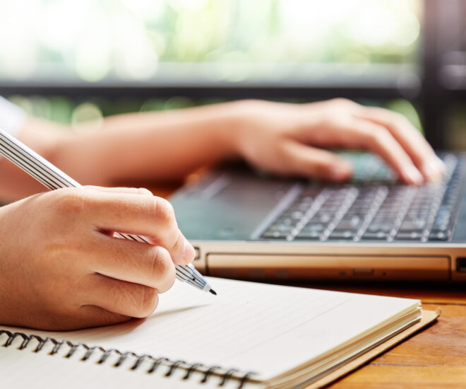 Person writing with right hand and typing with left hand