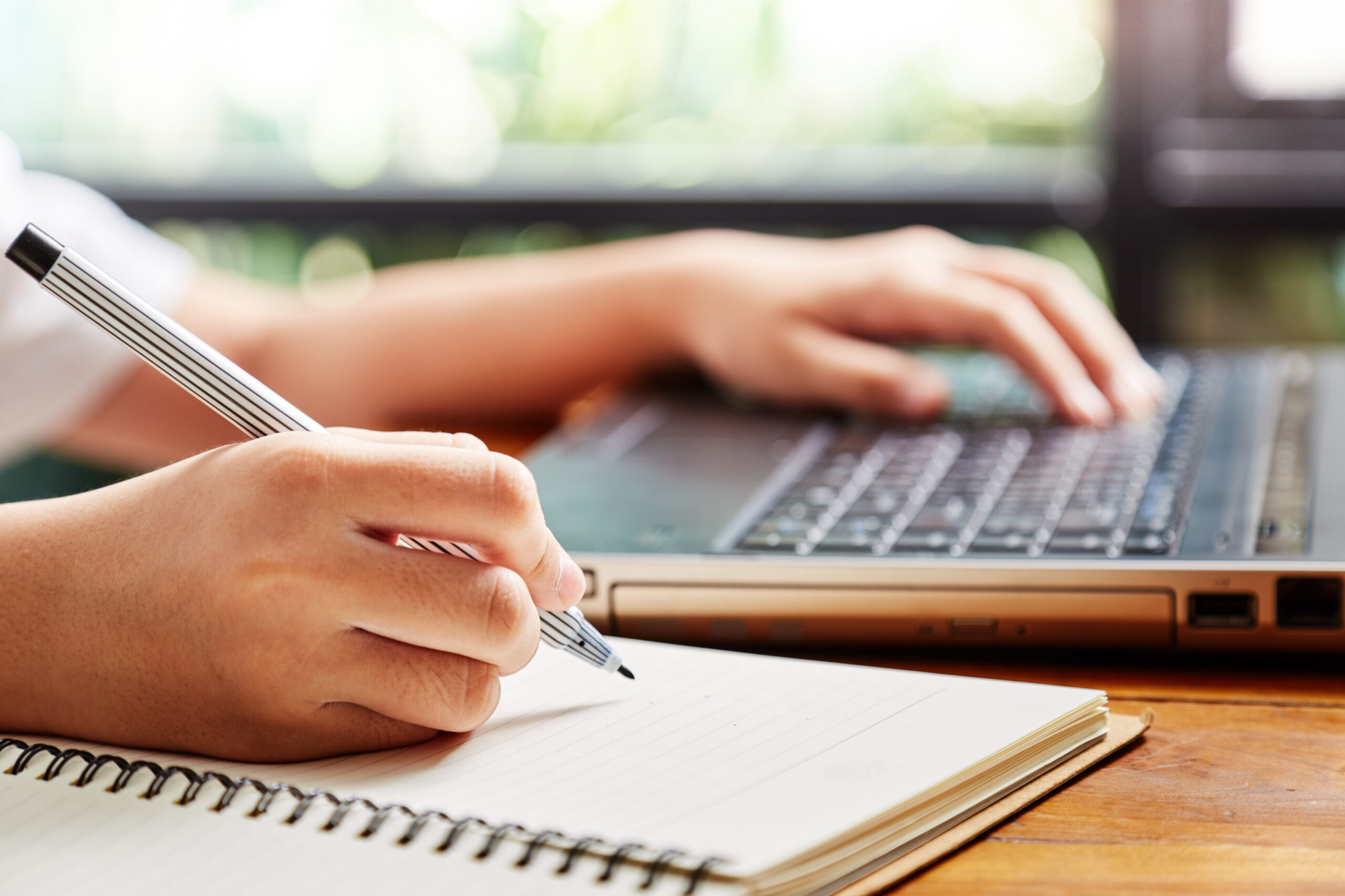Person writing with right hand and typing with left hand