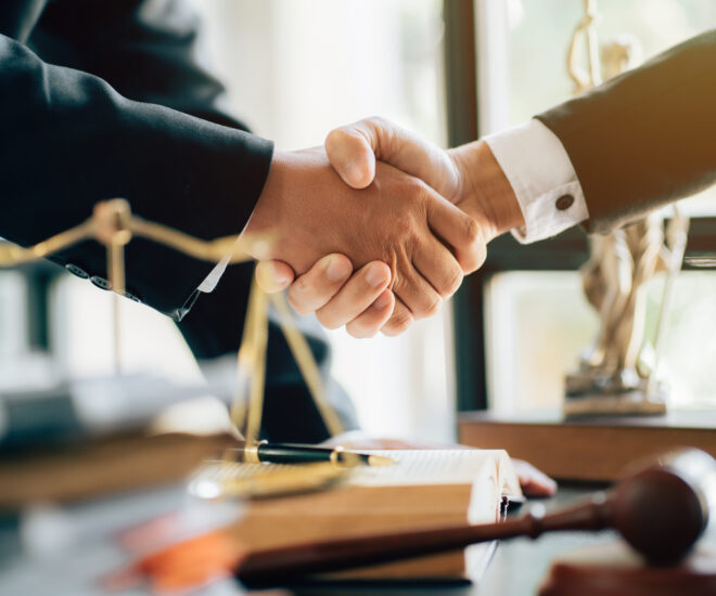Two people shaking hands over a desk with gavel and scales