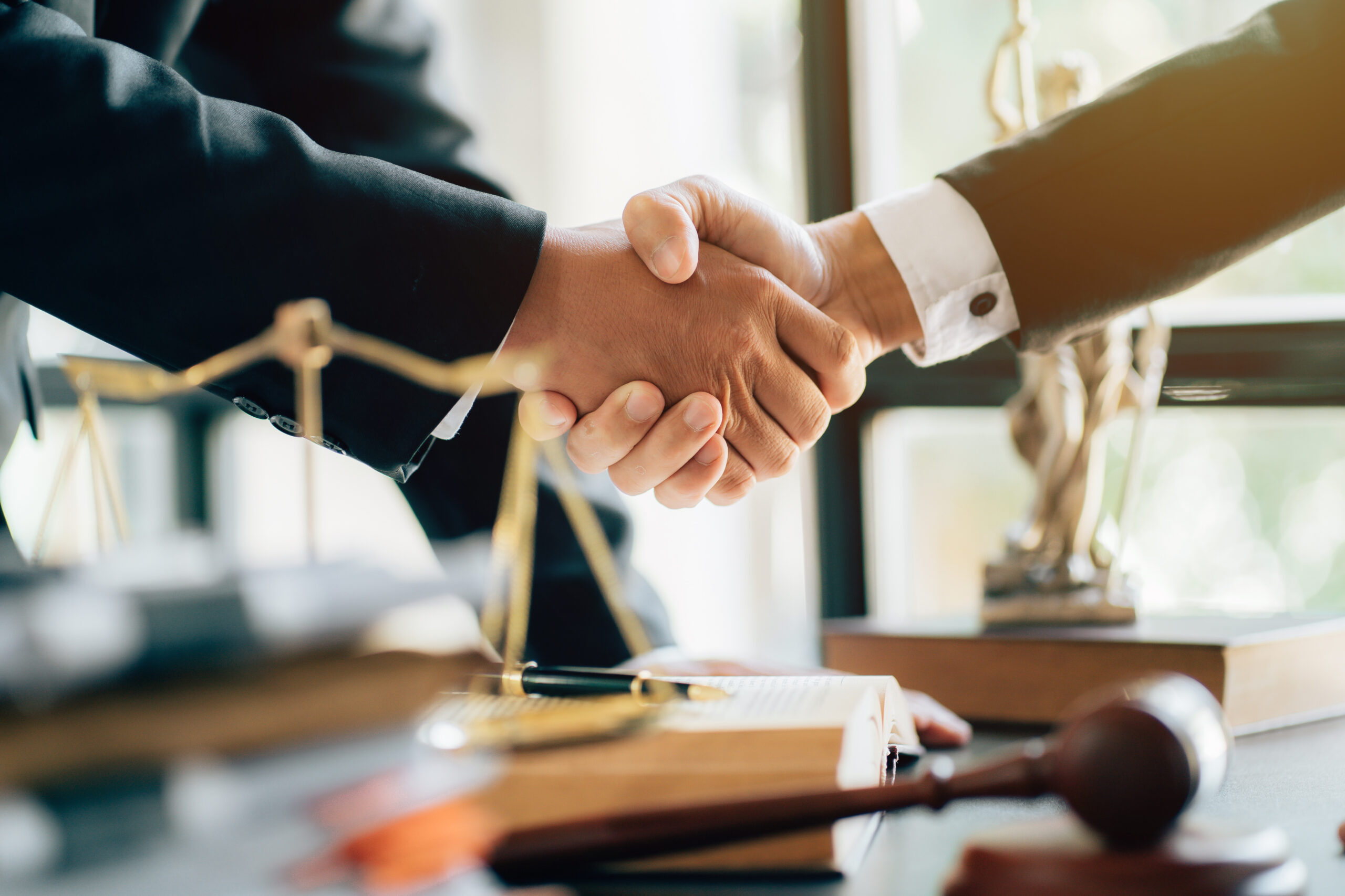 Two people shaking hands over a desk with gavel and scales