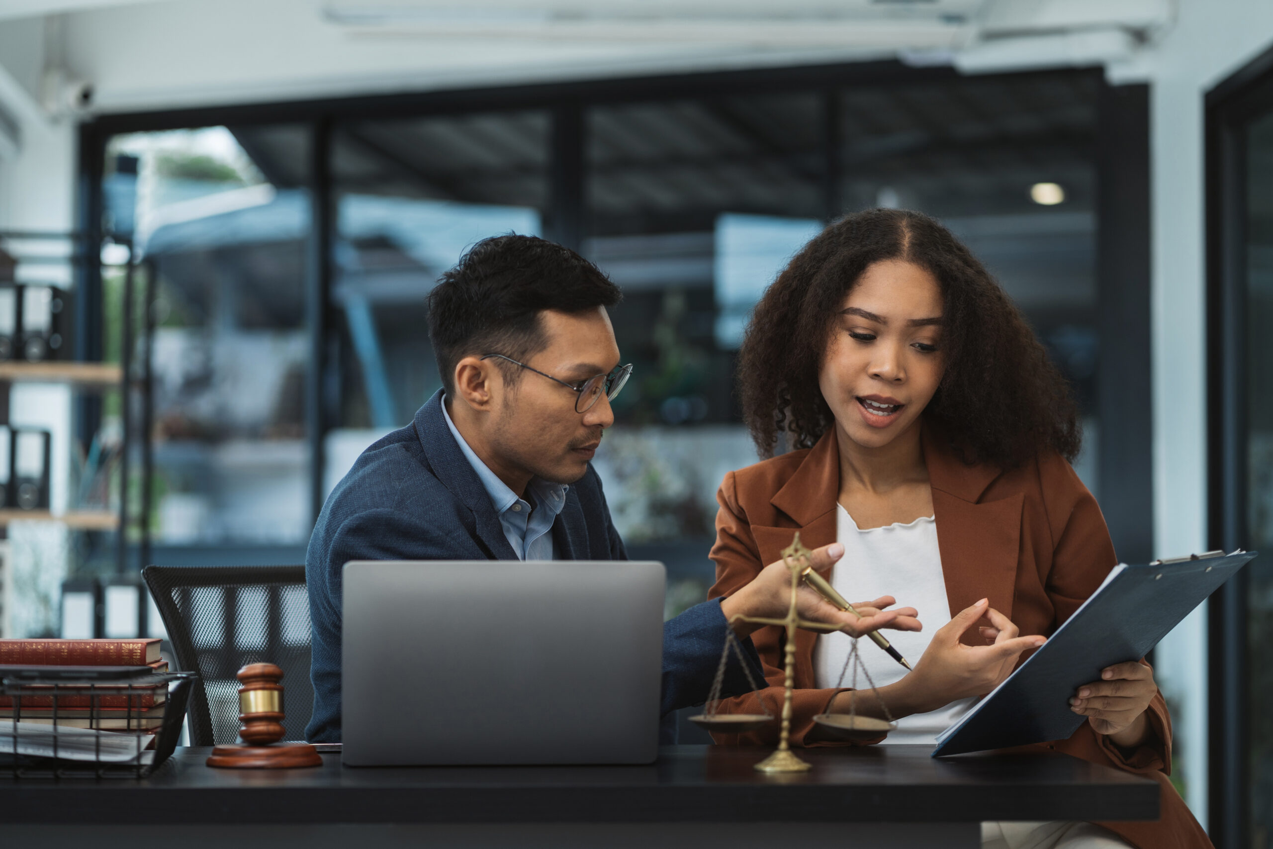 Business lawyer consulting with client at desk behind laptop, scales of justice, and judge's gavel.