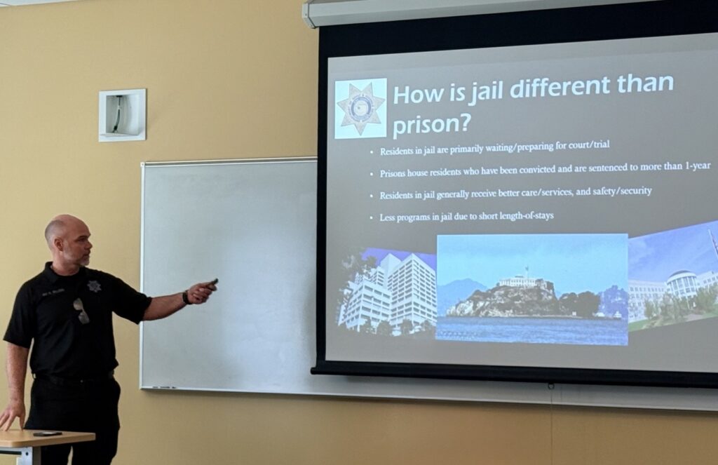 Speaker from King County Sheriff's Office in front of presentation about jails and prisons.