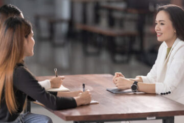 Two students holding pens sitting at table with advisor