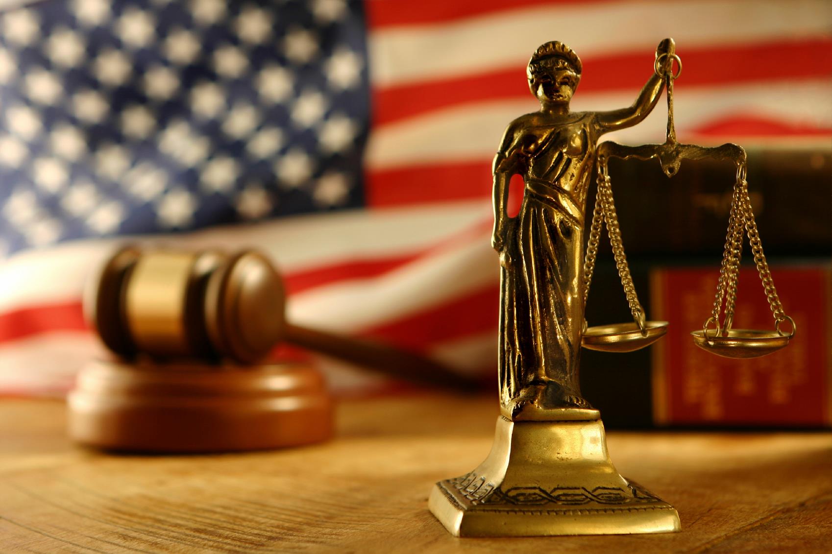 Lady justice with scales statue in front of gavel and American flag