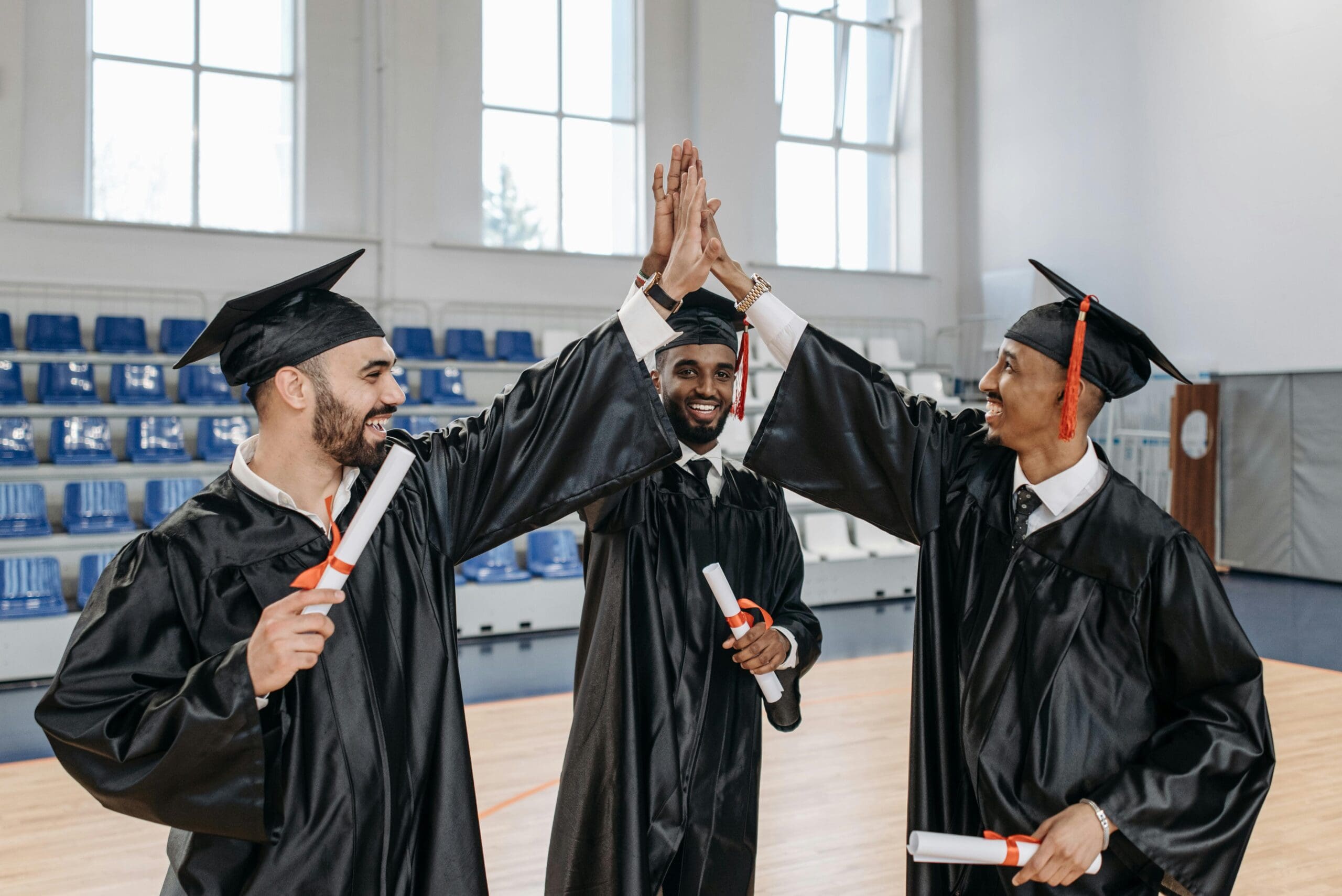 three students in cap and gown giving high five