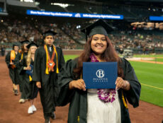 Students at graduation. A student holds a diploma while looking at the camera smiling.