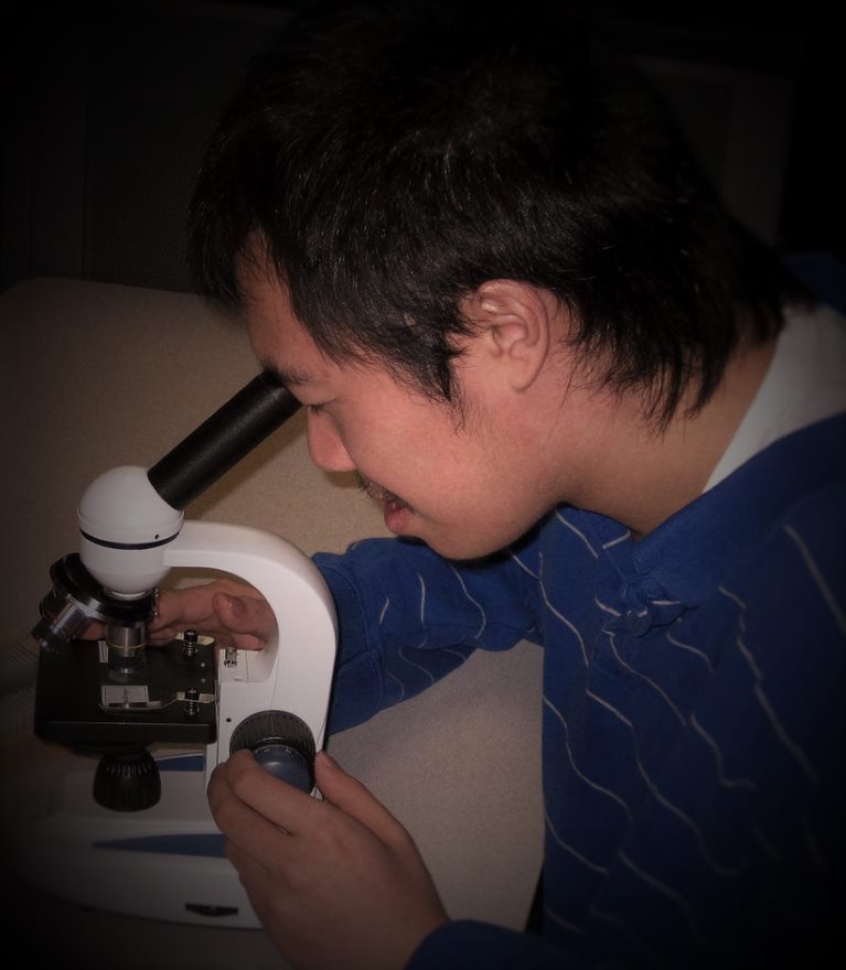 male-presenting student peering into a microscope