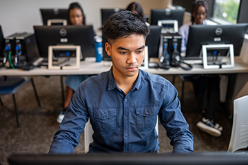 A student focuses on their computer while others also work at their computer stations.