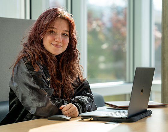 A smiling student looks up from their laptop.