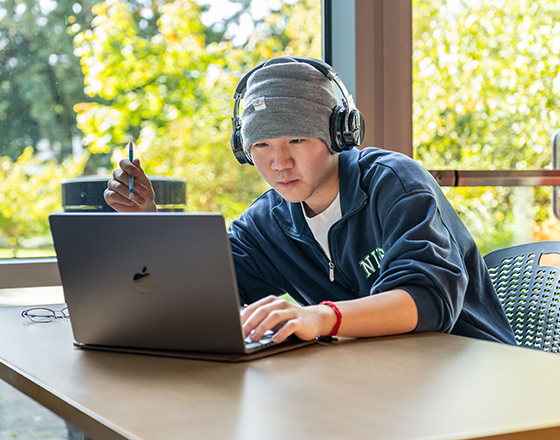 A student uses headphones and their laptop.