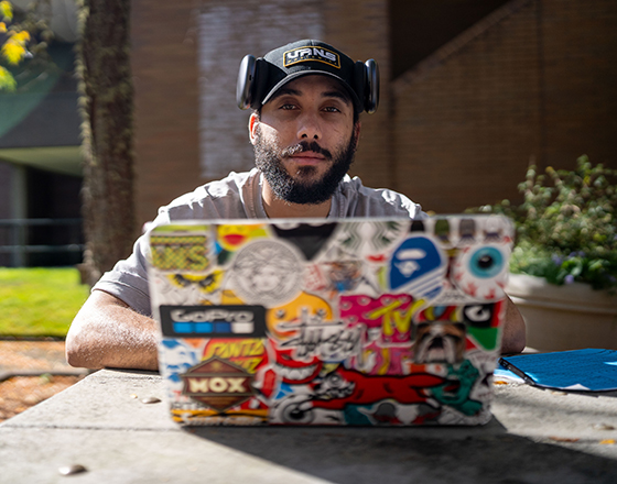 A student works outside on a stickered laptop.