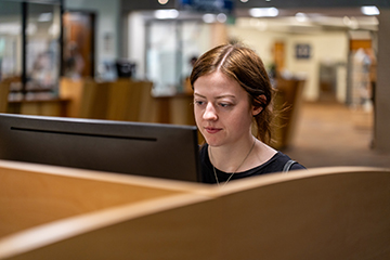 A student in a library study carrel concentrates on their computer screen.