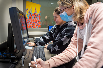 Students work on desktop computers while making notes.