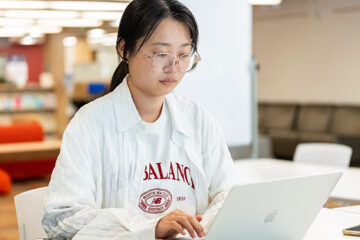 A student types on their laptop in a library setting.