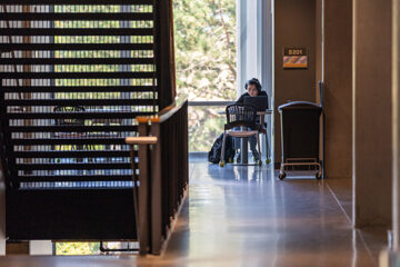 A student wears headphones and studies in the corner of a mezzanine by a large window.
