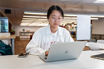 A student works on their laptop at a library table.