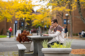 A student works on a laptop while sitting at a picnic table on the Bellevue College campus.