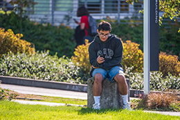 A student sits on campus while using their phone.