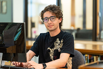 A student pauses while working on a desktop computer.