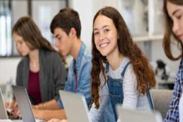 Students on the their laptops with a female smile toward the camera