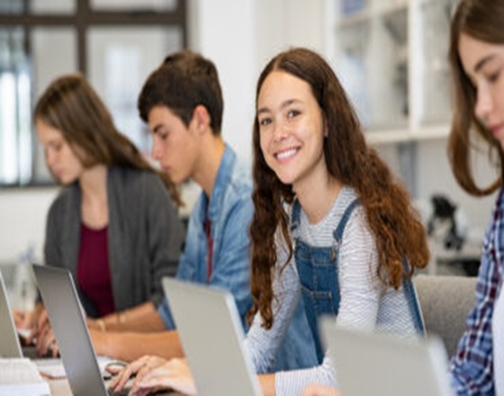 Students on the their laptops with a female smile toward the camera