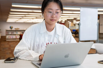 Students on the their laptops with a female smile toward the camera