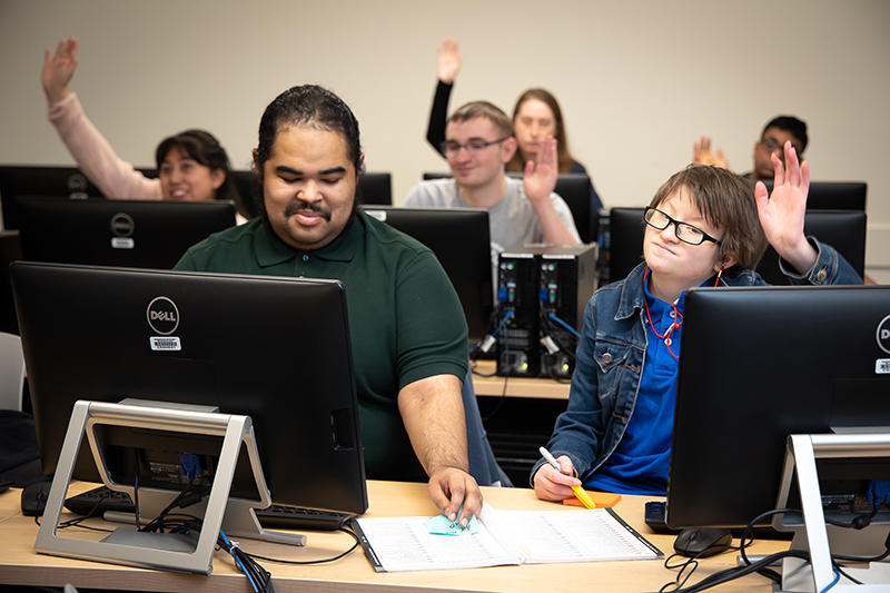 Occupational & Life Skills students raise their hands during class.