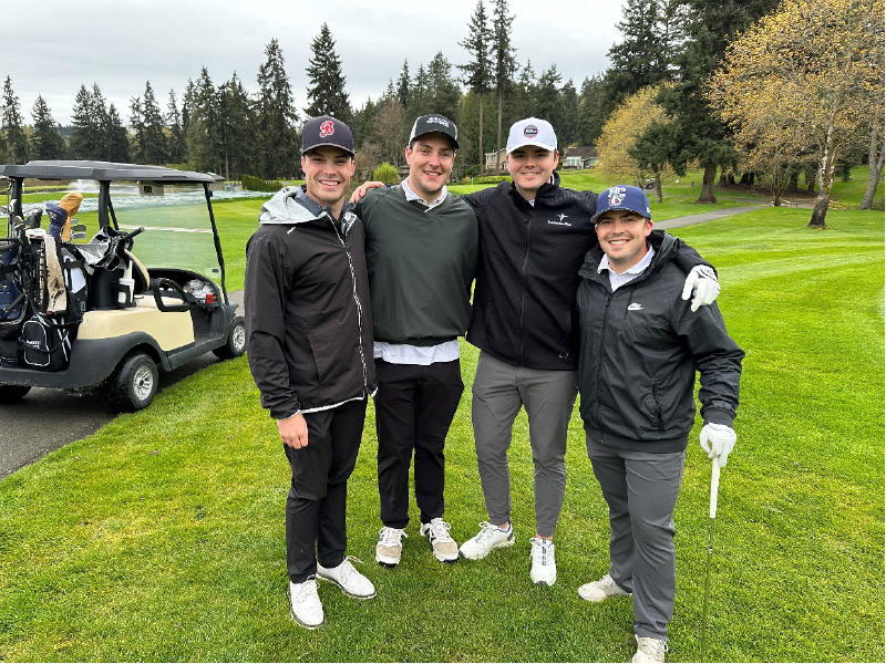 Four male golfers pose for a photo on golf course, with golf cart on left. Photo taken at 2024 Golf Scramble to support Bellevue College Athletics.
