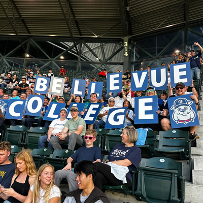 Alumni at Mariners game hold up signs spelling out Bellevue College