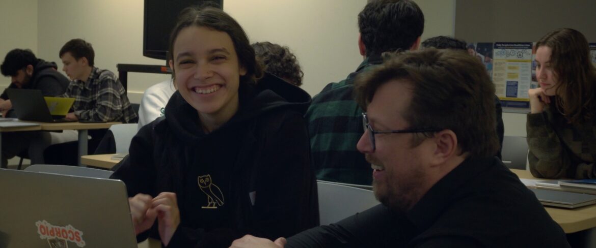 Student sitting on a table with FYS instructor, smiling.