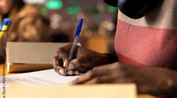 A person of color writing down on a piece of paper with a blue pen