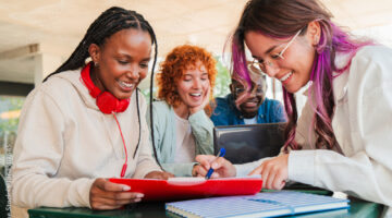 Three female students gathered together and working on something and smiling
