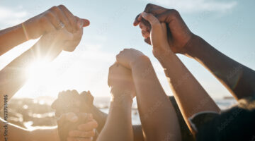 A group of people holding hands while the sun glares in the background