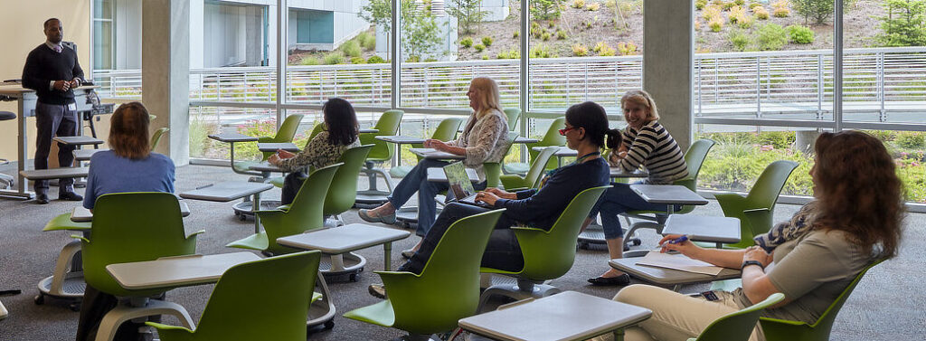 Students in class taking notes while teacher is presenting in the front of class.