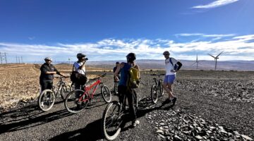 four people on a flat rocky road with their bikes on a clear day