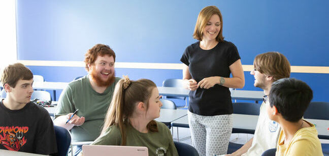 A teacher engaging with her 5 students in a classroom and everyone is in smiling