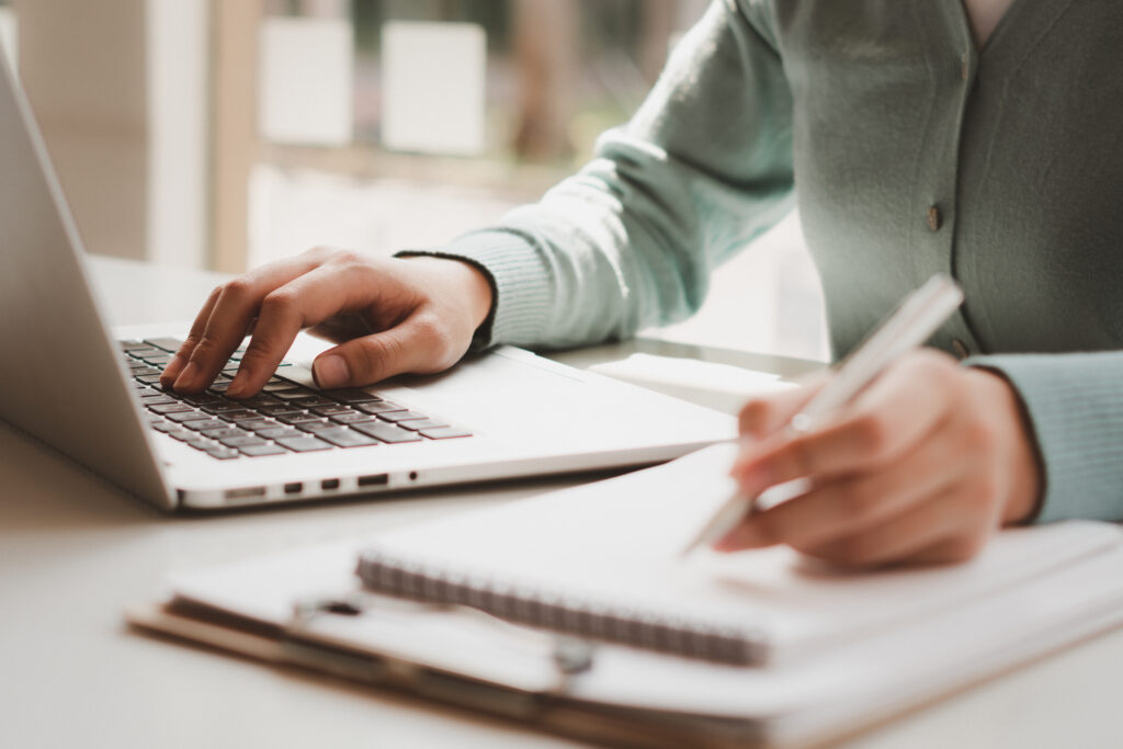 Image of person writing on a notepad while referring to a computer.