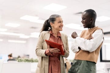 Older women with iPad smiling and talking to student, both seem quite happy.