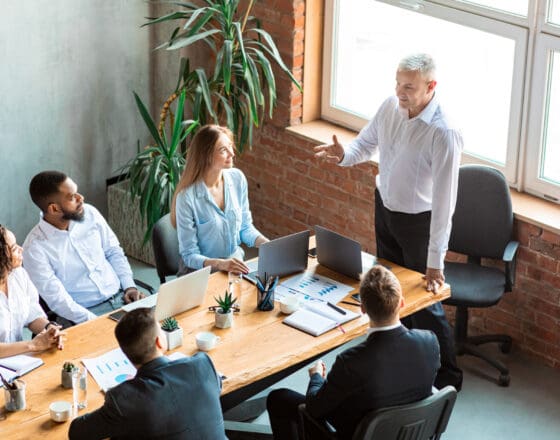 6 people sitting around a table in an office with everyone looking at the person who is standing