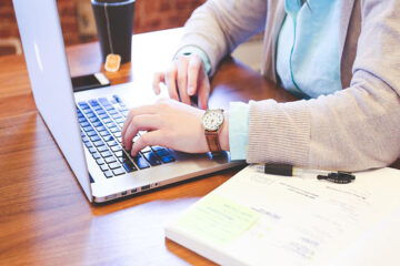 Hands typing on laptop sitting on desk, next to an open book and tea