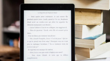 An eBook reader with French text in front of a stack of books